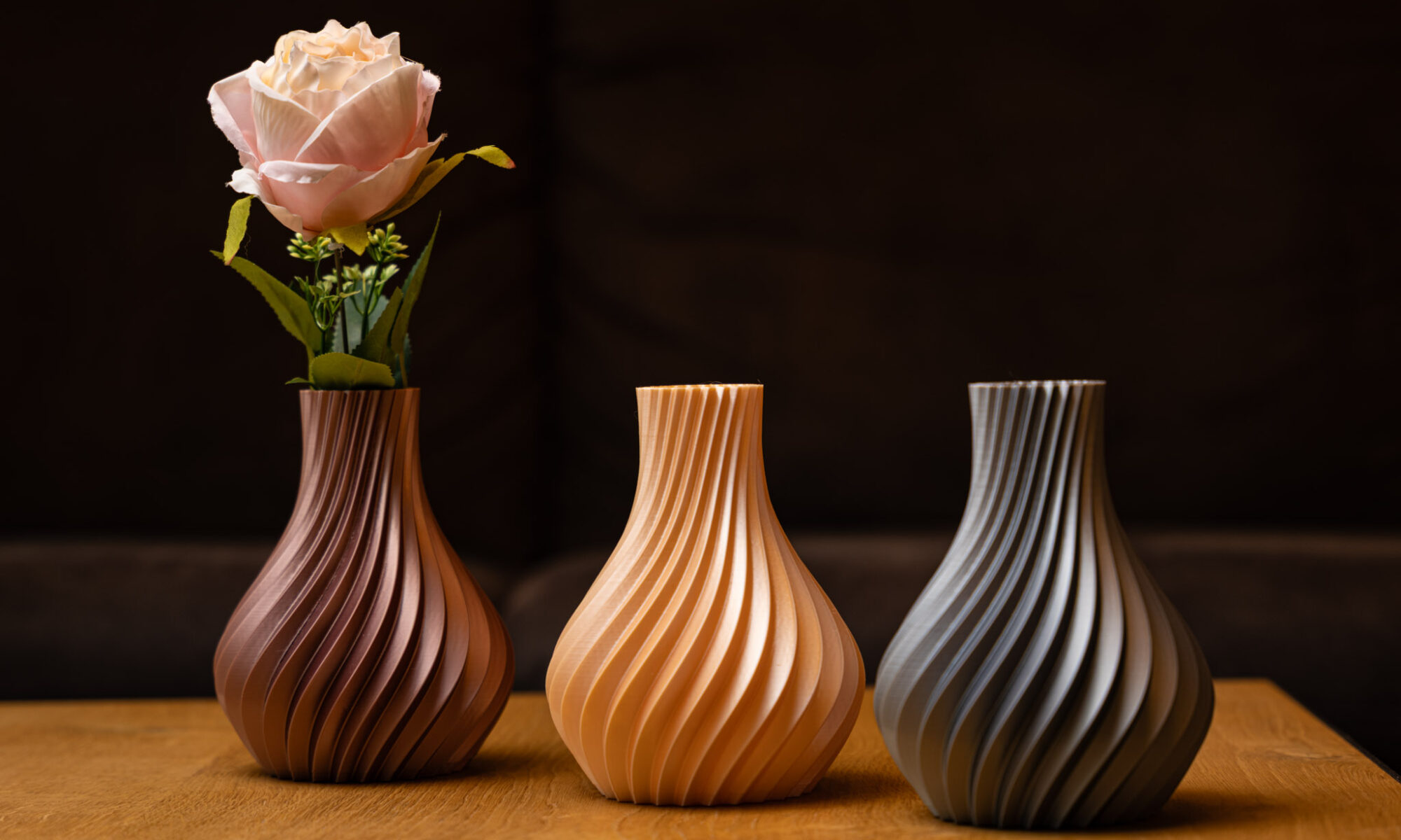Drei elegante 3D-gedruckte Vasen in Erdtönen zeigen geschwungene Designs auf Holz, perfekt für moderne Dekorationen.
