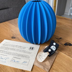 Blaue, gerippte 3D-gedruckte Vase auf Holztisch mit MyDesignStyle-Zertifikat und Schlüsselanhänger aus recycelten Materialien.