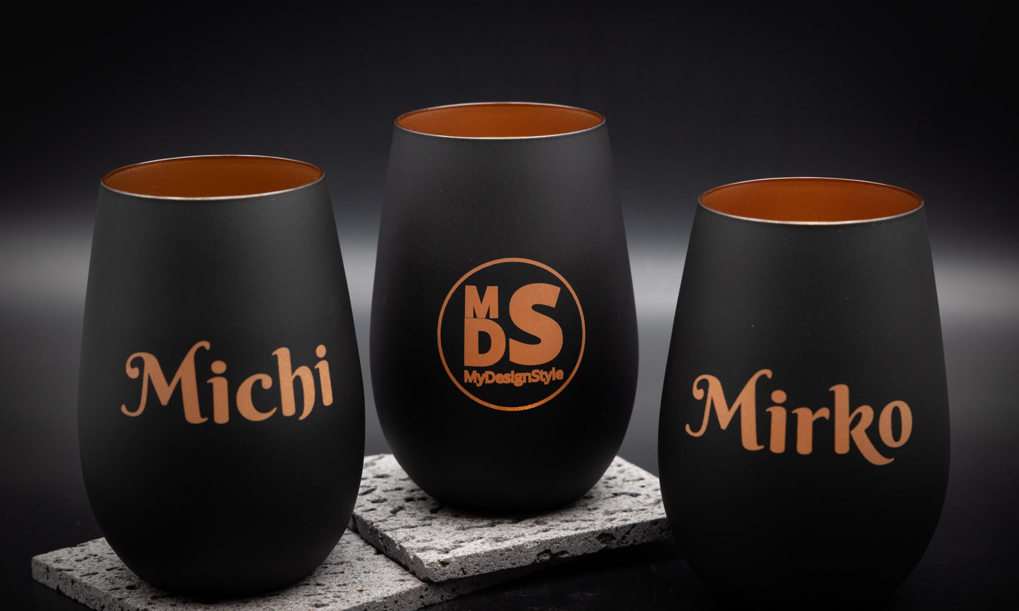 Drei elegante schwarze Becher mit personalisiertem Kupferdruck auf Steinuntersetzern; modernes Design von MyDesignStyle.